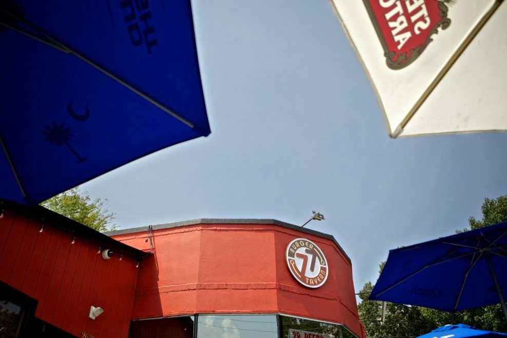 Outdoor patio umbrellas in front of the red Burger Tavern 77 building on Devine Street
